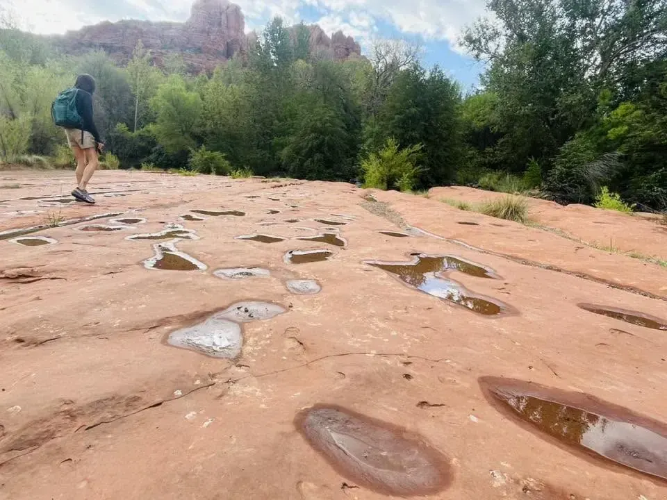 Hiker crossing red slickrock dotted with water pockets