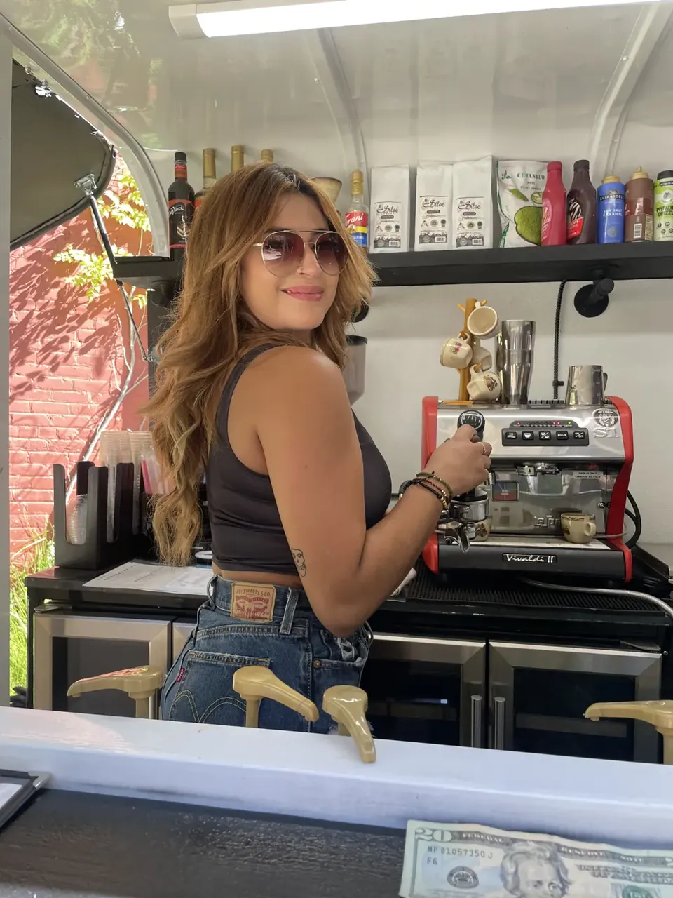 The barista at the coffee trailer, smiling over her shoulder at the espresso machine