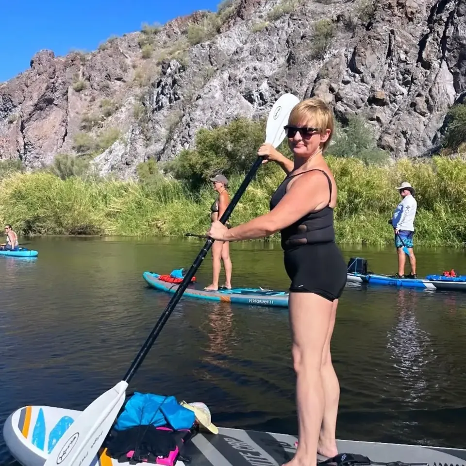 Paddleboarder on the river holding her paddle, more paddlers behind