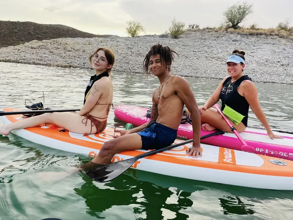 Three paddlers sitting on their boards at Saguaro Lake, smiling at the camera